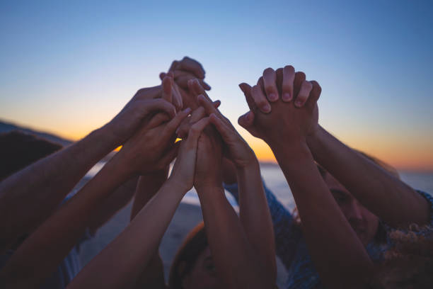 istockphoto-1301081602-612x612 Group of people holding hands in celebration and friendship. Multi ethnic and multi cultural group of young people holding their hands high outdoors on the beach. Shot is full of happiness, success and energy with several ethnic backgrounds including African and Caucasian.